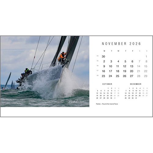 A sailboat with crew racing through choppy water is featured on the Rick Tomlinson Desk Calendar 2026 by Rick Tomlinson Photography, with a November page and adjacent months shown—an image by the renowned yachting photographer.