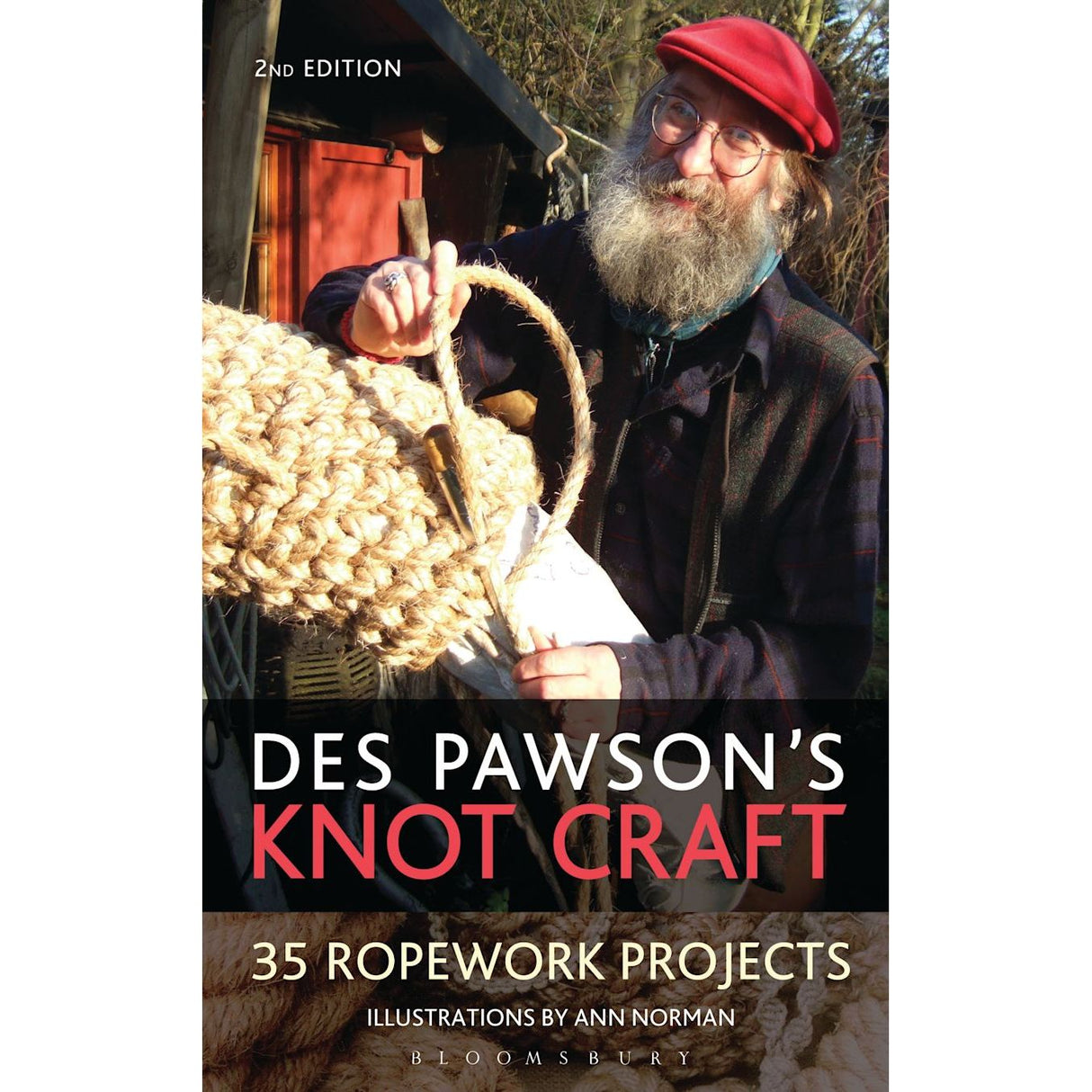 A bearded person in a red beret smiles while demonstrating ropework next to a large woven knot on the cover of "Des Pawson's Knot Craft" by renowned author Des Pawson, published by Adlard Coles.