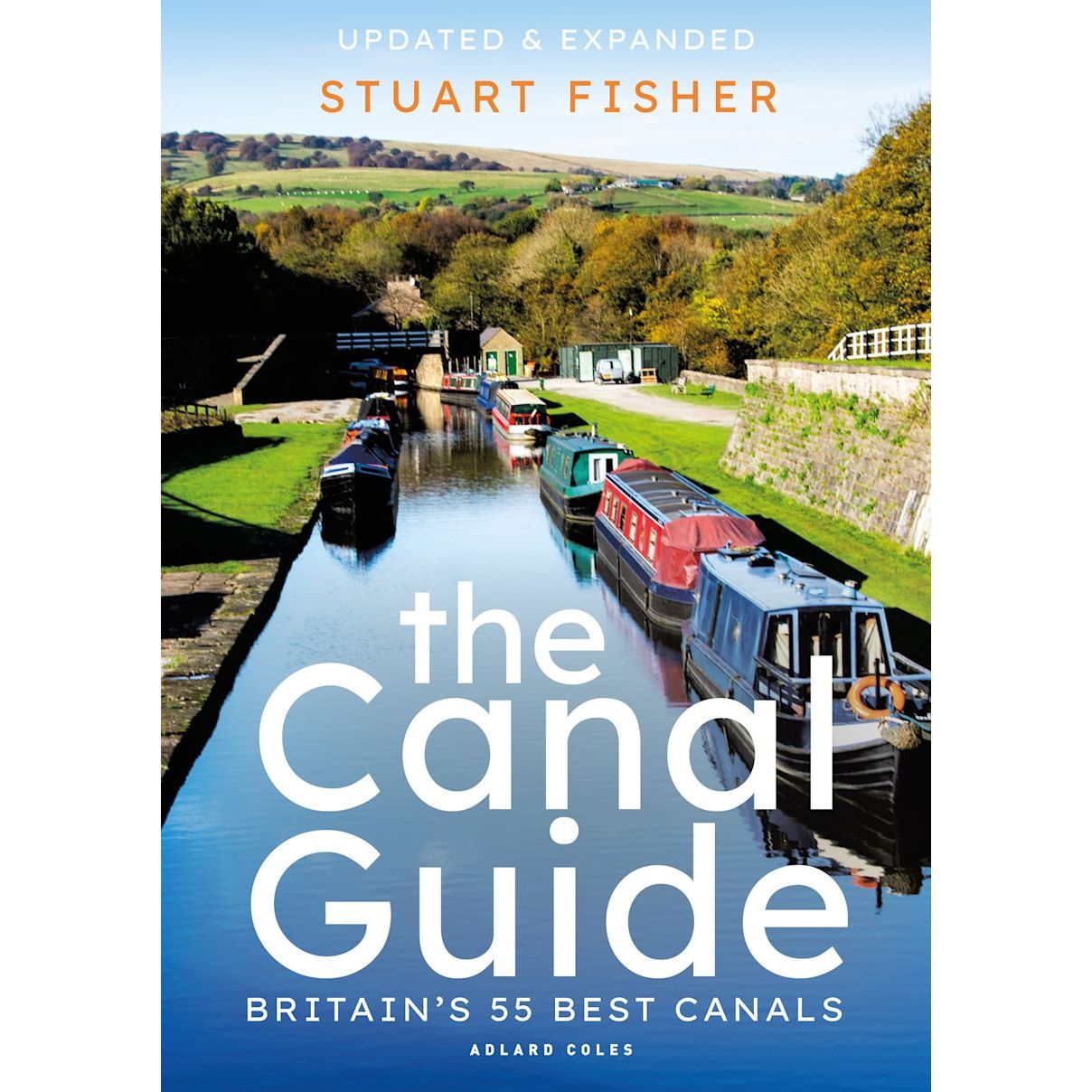 The cover of "The Canal Guide" by Stuart Fisher, published by Adlard Coles, features vibrant narrowboats sailing a sunlit canal surrounded by lush greenery. It highlights "Updated & Expanded" and "Britain’s 55 Best Canals," making it an essential guide to Britain's waterways heritage.