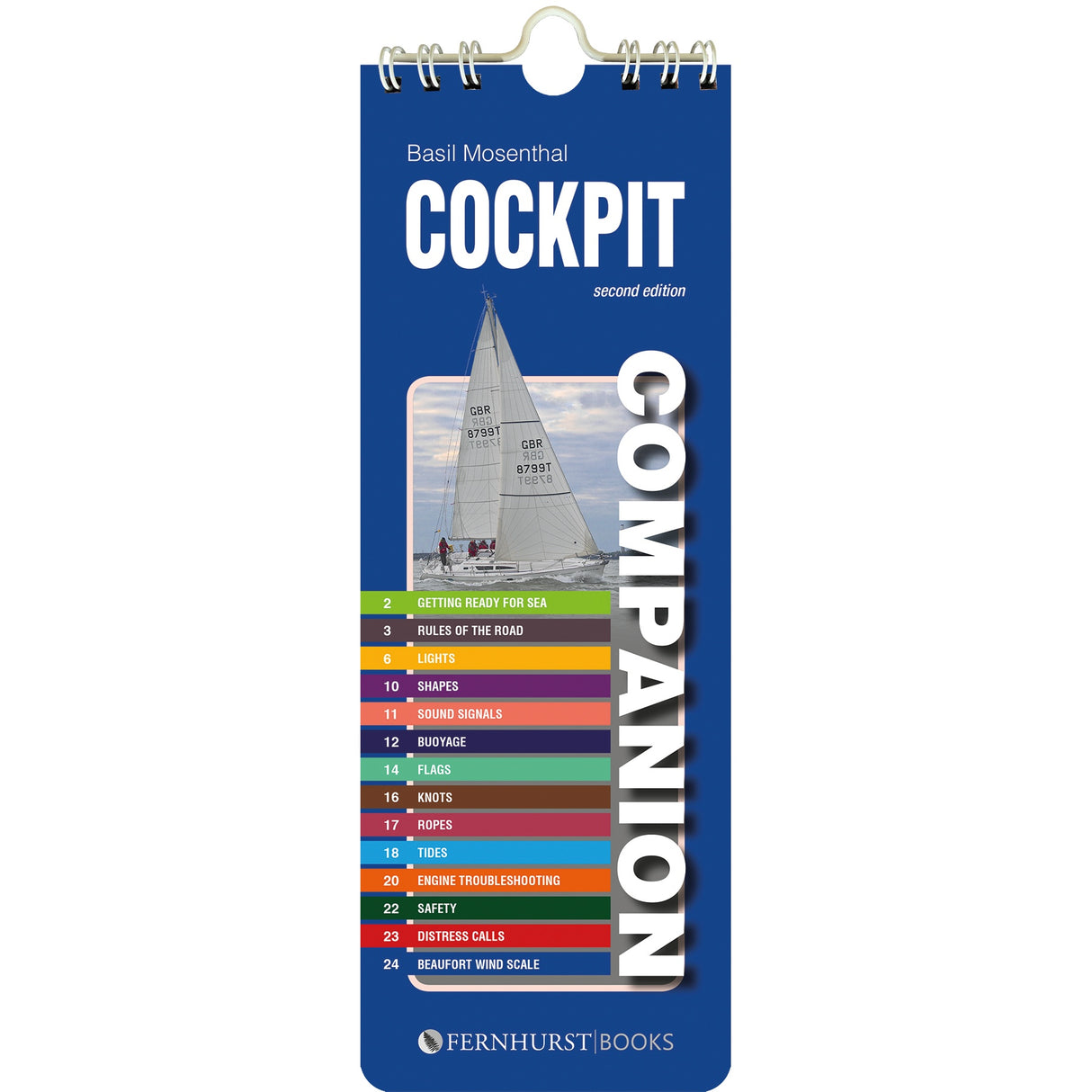 The "Cockpit Companion" by Fernhurst Books is a blue spiral-bound cruising reference booklet, featuring a sailboat and a colorful seamanship index—covering topics like lights, buoys, knots, safety, and distress calls—on its cover.