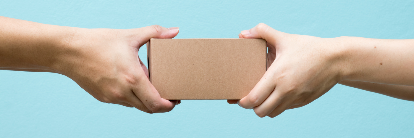 Two hands extending towards each other to pass a small cardboard box against a light blue background.