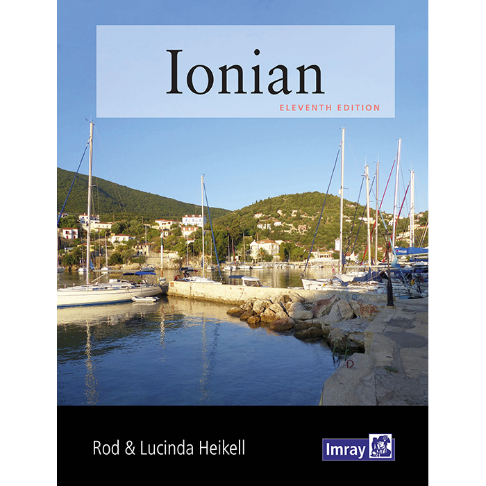 The cover of the Imray "Ionian" guide features sailboats in a tranquil harbor against green hills and houses. The bold title and authors Rod & Lucinda Heikell emphasize its reputation as a trusted resource for Greek cruising.