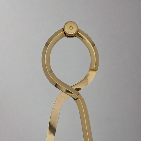 Resembling a minimalist sculpture, the Chartwright 7" Single-Handed Brass Dividers feature polished metal strands intertwined to form a loop at the top, evoking an abstract human figure. Set against a plain gray background that highlights their reflective brass surface, these dividers combine modern elegance with the precision reminiscent of fine instruments.