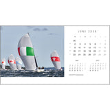 Sailboats race in the ocean under spinnakers with international designs, featuring green and red stripes. Captured by renowned yachting photographer Rick Tomlinson, this vibrant image is showcased in the Rick Tomlinson Photography Desk Calendar 2025, highlighting the months of May, June, and July.