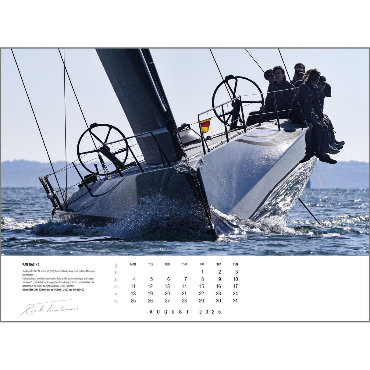 A sleek yacht glides through the water with several people sitting on the side, captured in a captivating image from the Rick Tomlinson Portfolio Calendar 2025 by Rick Tomlinson Photography. This photo graces an August 2025 page, featuring large black spiral wheels on the yacht and a signature at the bottom left, epitomizing sailing photography.