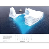 A sailboat sails by a huge iceberg with vivid blue underwater hues. The Rick Tomlinson Photography Rick Tomlinson Portfolio Calendar 2026 showcases this stunning March scene with icy whites and deep blue ocean.