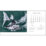 A striking aerial of a sailboat on green waters highlights the June 2026 page of the Rick Tomlinson Desk Calendar from Rick Tomlinson Photography, with small calendars for May and July and iconic yachting photography throughout.