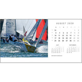 Two sailboats race across the water, their sails billowing. On the right is the Rick Tomlinson Desk Calendar 2026 by Rick Tomlinson Photography, open to August with stunning yachting imagery; July and September mini calendars are shown below.