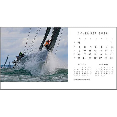 A sailboat with crew racing through choppy water is featured on the Rick Tomlinson Desk Calendar 2026 by Rick Tomlinson Photography, with a November page and adjacent months shown—an image by the renowned yachting photographer.