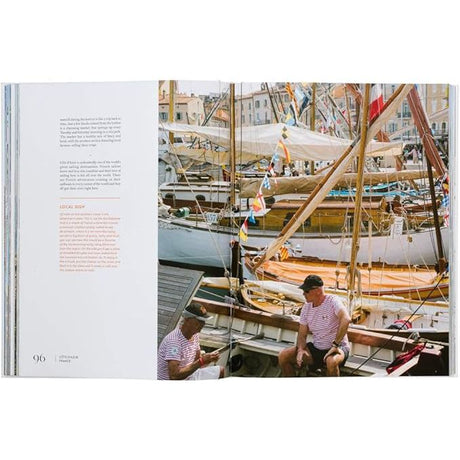 The open spread of "Sailing the Seas" by gestalten highlights text about a local dock on the left and a right-page photo of two striped-shirted individuals on a boat. The scene captures a bustling harbor filled with masts and vibrant flags flapping in the wind.