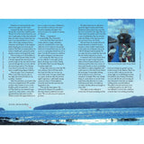 A two-page spread from "Under Wide and Starry Skies" by Adlard Coles overlays a scenic ocean view with mountains. It features text and an image of people by a boat in a tropical setting, hinting at remote sailing locations. Sunlit sparkling water invites thoughts of yacht escape adventures.