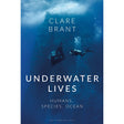 The book cover for "Underwater Lives" from Bloomsbury features a diver gliding beside a manta ray amidst deep blue ocean waters, illuminated by sunlight streaming overhead. Combining underwater life writing with reflections on ocean sustainability, the cover’s subtext states: “Humans, Species, Ocean.”.