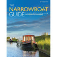 Cover of "The Narrowboat Guide" by Tony Jones, Adlard Coles. The Second Edition depicts a narrowboat gliding along a tranquil canal under a cloudy blue sky, surrounded by lush greenery and softly illuminated by sunlight, capturing the essence of the liveaboard experience.