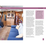 Experience the relaxing liveaboard lifestyle with The Liveaboard Guide by Adlard Coles—enjoy wood floors, a blue sofa with cushions, a wooden cabinet, and sunlit circular windows for a cozy boat interior.