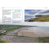 A sandy beach curves along the shoreline of St Bees, backed by green hills and a bustling promenade. After Lake District kayaking with Paddle the North of England by Adlard Coles, explore local highlights shown in info boxes under a cloudy sky.
