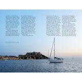 A white sailboat glides on tranquil water by a historic French town with stone buildings and a hilltop fortress. "Floating Through France" by Adlard Coles appears in text on the left, evoking perfect evening cruising scenes.