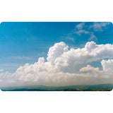 Large, puffy white clouds from The Cloud Deck by David & Charles drift against a bright blue sky above a distant, rolling landscape.