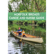 A man and a child paddle a canoe along a peaceful, tree-lined river in the picturesque Norfolk Broads. The book cover displays "Norfolk Broads Canoe and Kayak Guide" by Steve Maloney, published by Pesda Press, providing expert guidance on the top paddling routes across this scenic area.