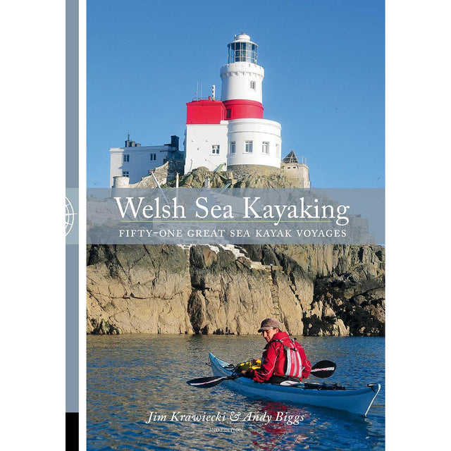 A kayaker paddles along a rocky shoreline beneath a white and red lighthouse under a clear blue sky. Text reads: "Welsh Sea Kayaking" by Pesda Press—your essential guide to 51 great sea kayak voyages for exploring the stunning Welsh coastline.
