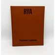 The Royal Yachting Association's RYA Personal Logbook, a brown hardcover, stands upright against a white background—ideal for documenting your journey as a Coastal Skipper or Yachtmaster.