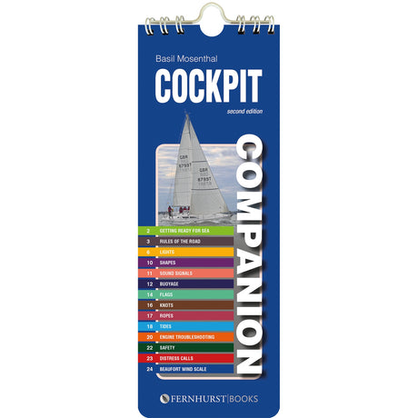 The "Cockpit Companion" by Fernhurst Books is a blue spiral-bound cruising reference booklet, featuring a sailboat and a colorful seamanship index—covering topics like lights, buoys, knots, safety, and distress calls—on its cover.