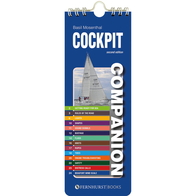 The "Cockpit Companion" by Fernhurst Books is a blue spiral-bound cruising reference booklet, featuring a sailboat and a colorful seamanship index—covering topics like lights, buoys, knots, safety, and distress calls—on its cover.