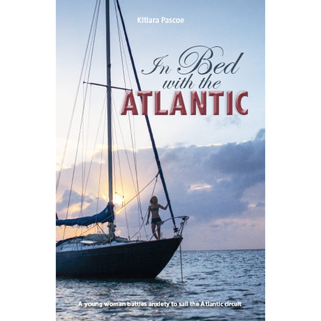 At sunset, a woman stands on a sailboat’s bow with calm water and clouds around her. The book cover reads: "In Bed with the Atlantic" by Fernhurst Books—a travel memoir about overcoming anxiety through sailing.