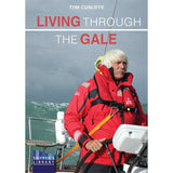 A man in a red jacket stands at the helm of a sailboat in rough seas, with "Living Through The Gale" by Fernhurst Books displayed above him, capturing the spirit of heavy weather sailing.