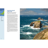 Experience the thrill of sailing past rocky cliffs, a sea arch, and distant lighthouse at Land’s End, England with Fernhurst Books’ Ultimate Sailing Adventures under a bright sky above blue ocean waves.