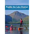 Two people paddle across a mountain-framed lake—one in a kayak, one on a paddleboard—beneath the title "Paddle the Lake District" by Pesda Press. This comprehensive kayaking guidebook uncovers the top paddling locations and picturesque canoe routes in the Lake District, offering explorers an essential companion for memorable adventures on these iconic waters.