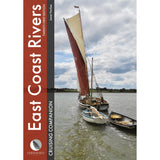 A sailboat with a large reddish-brown mainsail towing two small wooden dinghies on a river, as featured in the East Coast Rivers Cruising Companion by Fernhurst Books.
