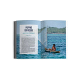 Open magazine featuring an article titled "Prepping for Passage" along with a photo of a person navigating a small wooden boat equipped with a sail across calm blue waters. With trees visible under the clear sky in the background, this scene is ideal for ocean-loving foodies and liveaboard cruisers alike. Discover more within "The Hunter & The Gatherer" by Exploring Eden Media.