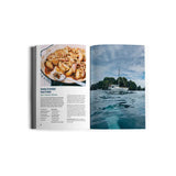 An open book, titled "The Hunter & The Gatherer" by Exploring Eden Media, showcases a sustainable recipe for peach crumble with a photo on the left page. On the right page, there's an image of a sailboat gliding across a clear blue sea—ideal for ocean-loving food enthusiasts exploring scenic routes alongside rocky, lush islands.