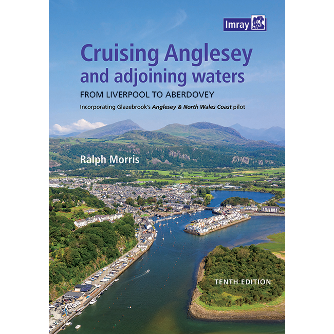 Aerial view of a coastal town with a river winding through green hills under blue sky. Book cover: "Cruising Anglesey and Adjoining Waters" by Imray—an essential North Wales coast guide for pilots. Imray logo top right.