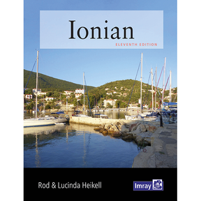 The cover of the Imray "Ionian" guide features sailboats in a tranquil harbor against green hills and houses. The bold title and authors Rod & Lucinda Heikell emphasize its reputation as a trusted resource for Greek cruising.