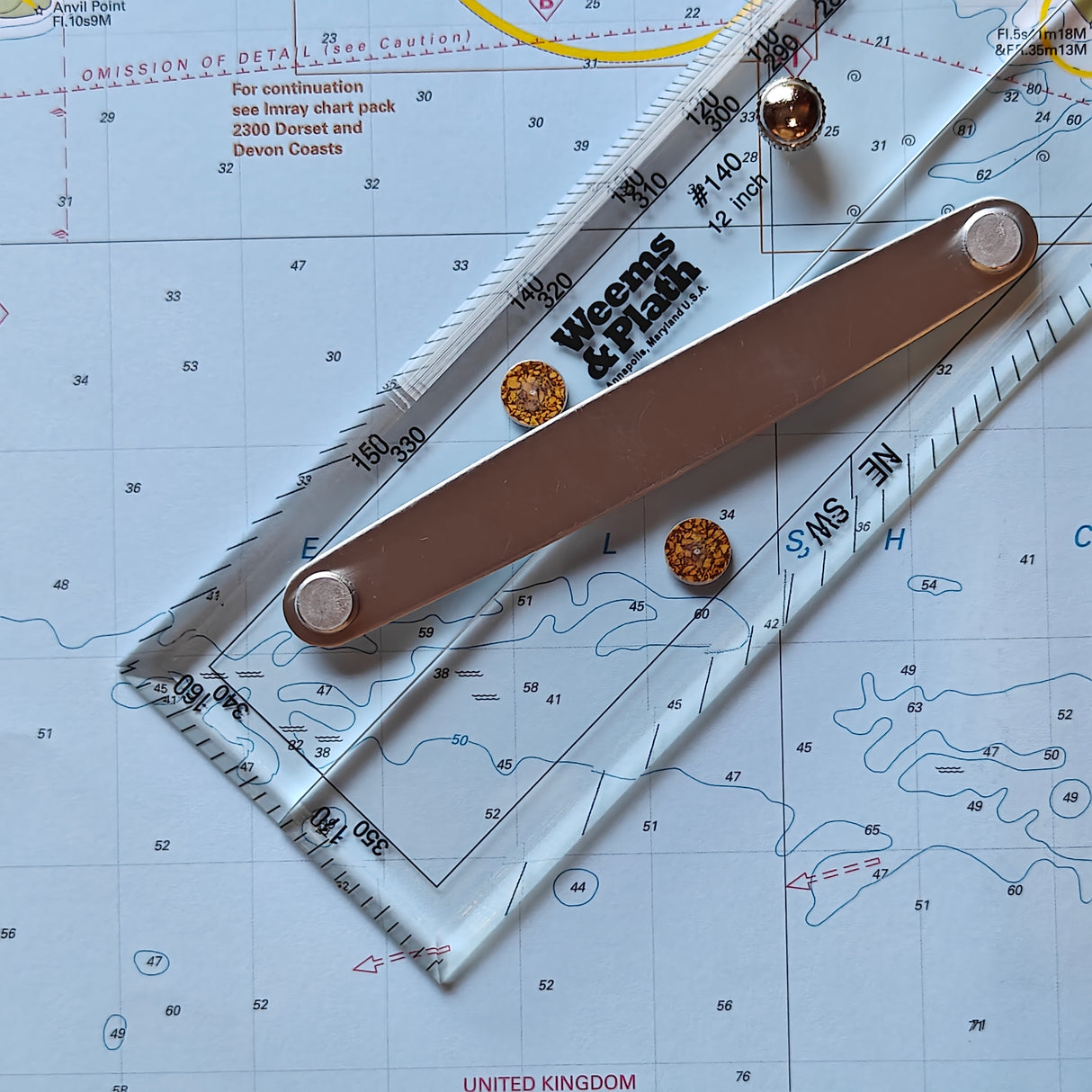 A navigation chart featuring a durable Weems & Plath 12" Parallel Rule and brass screws rests on the United Kingdom's coastal waters. The chart includes depth contours, labels such as "Venus & Plum," coordinates, and various geographical features marked with precision.