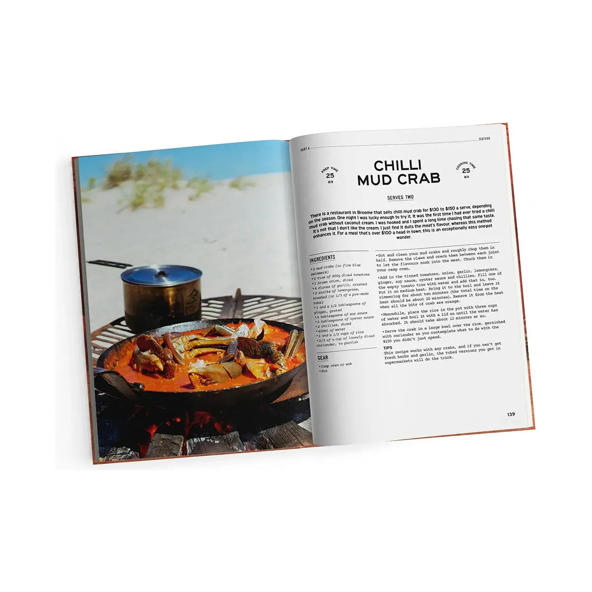 An open copy of "Fire to Fork" from Exploring Eden Media sits on a sandy beach, showcasing a recipe for "Chilli Mud Crab." On the left page, there's an image of campfire cooking on an outdoor grill; the right page details the ingredients and cooking instructions. In the background, a small pot emphasizes the spirit of outdoor cuisine.