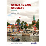 Cover of the book "Germany & Denmark," first edition by Imray. It depicts a sailing odyssey with a harbor scene featuring boats, vibrant buildings, and a church with a tall spire under a cloudy sky. The logos of the Royal Cruising Club Pilotage Foundation and Imray are displayed prominently.