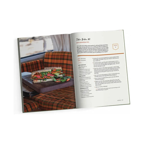 A copy of *The Small Kitchen Cook* by Exploring Eden Media is open to a Tofu Bánh Mì with Lemongrass Pâté recipe. On the left page, there's an image of the sandwich on a wooden tray against a plaid seat backdrop. The right page details the ingredients and instructions, making it perfect for small kitchen cooks eager to experiment with creative cooking techniques.