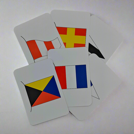 The Flip Cards - International Code Flags by Flip Cards are presented in a fanned arrangement. This set includes six rectangular cards, each featuring a unique and vibrant nautical signal flag from the International Code of Signals. The flags boast diverse designs such as stripes, triangles, and cross patterns, all showcased on a flat, plain surface.