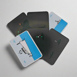 Five Flip Cards - Lights and Shapes are spread out in a fan shape on a grey surface. The cards feature minimalist illustrations of a boat with navigation lights against a blue and white background, while their black backs display small colored dots and abstract shapes.