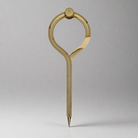 The Chartwright 7" Single-Handed Brass Dividers stand upright on a neutral gray background, showcasing their elegant and streamlined design. This precision instrument features a single pointed leg and a circular grip at the top, offering a modern and minimalist appearance reminiscent of classic brass dividers used for chart work.