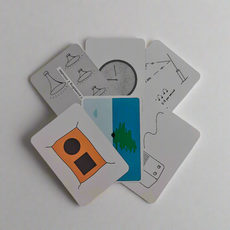 A fan of six Flip Cards - Sound and Light Signals, from the Flip Cards brand, features minimalist illustrations on a white surface. The top card displays an orange rectangle, while the others show simple line drawings like a clock, musical notes, and abstract shapes. The backs of the cards are plain white.