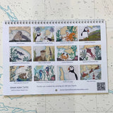 The Hannah Wisdom Textiles Coastal Calendar 2026 features twelve textile art illustrations of coastal animals and scenes, each marked with a location, set against a nautical map background.