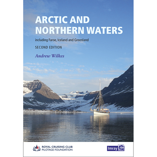 The cover of Imray's "Arctic and Northern Waters" by Andrew Wilkes features a sailboat on a tranquil, reflective body of water surrounded by snow-capped mountains under a clear sky. This Arctic guidebook is the second edition and includes information on the Faroe Islands, Iceland, and Greenland.