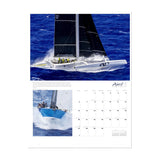 A page from the Sharon Green Ultimate Sailing 2025 Calendar for April features two breathtaking images. At the top, a white and black sailboat elegantly navigates the ocean, while underneath, a blue sailboat leans with its mast tilted gracefully. The calendar dates are stylishly positioned on the right side of the page.